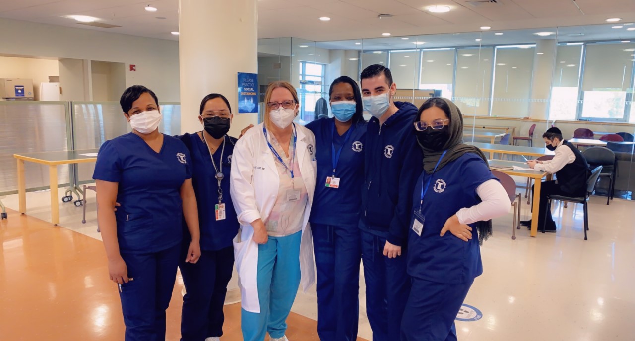 Five nursing students in scrubs stand with a female faculty member