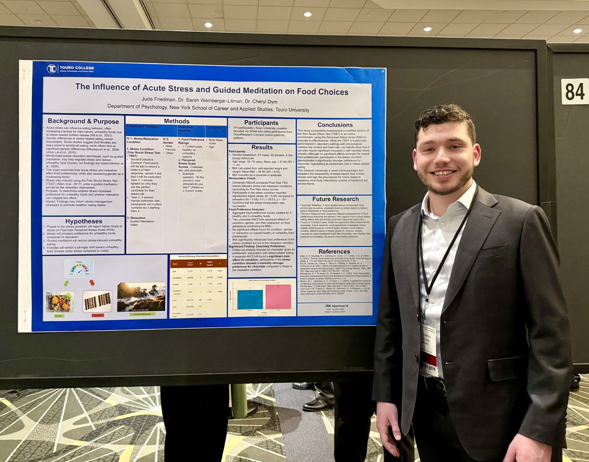 Juda Friedman wearing a suit and standing in front of research poster presentation.