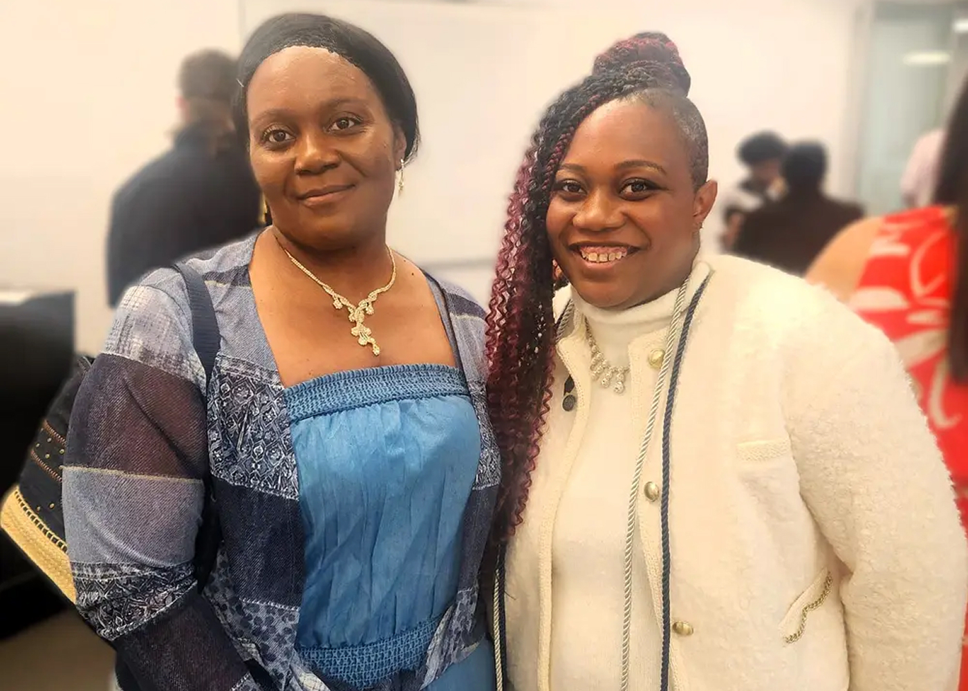 Two African American women standing together, one is wearing a blue dress and the other is wearing a white outfit.